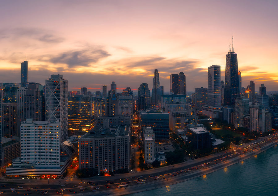 Lake Shore Drive curves away under a violet dusk, the lights of the Chicago lakefront coming on one by one