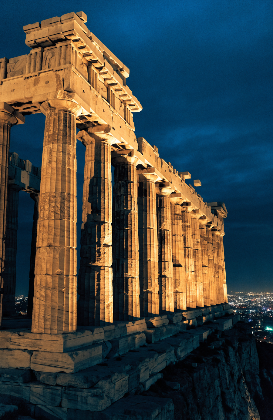 The columns of the Parthenon stand lit in warm gold above Athens, the city spread out far below