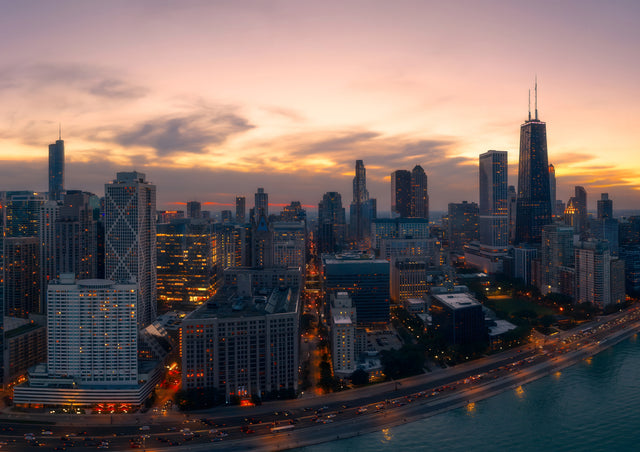 Lake Shore Drive curves away under a violet dusk, the lights of the Chicago lakefront coming on one by one