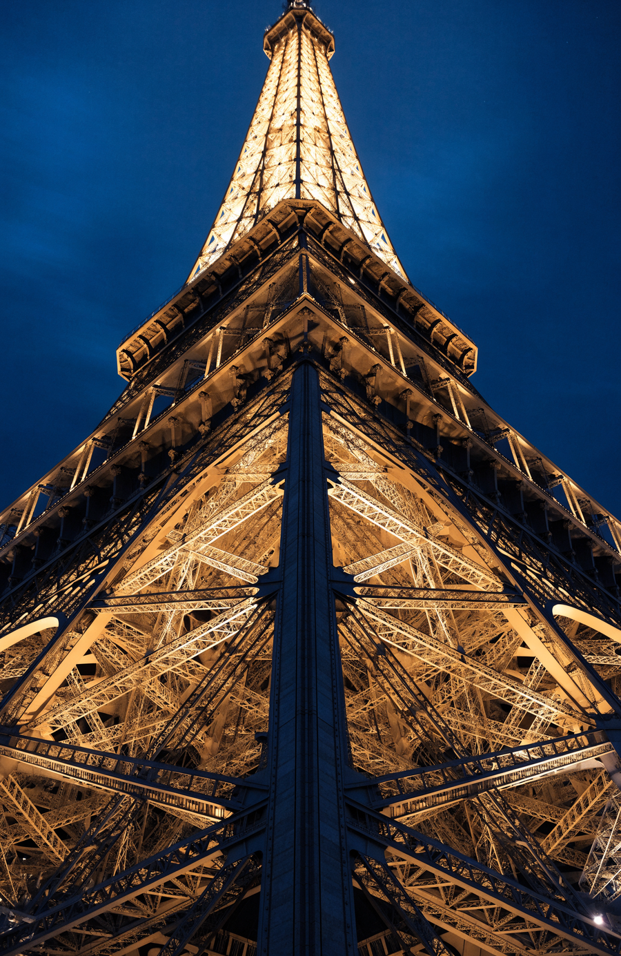 The Eiffel Tower climbs the whole frame in warm gold ironwork against a deep blue Paris night