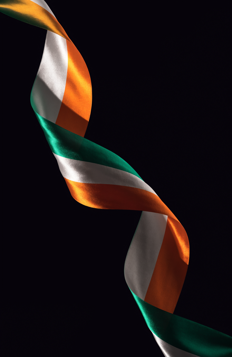 A ribbon of silk in Irish green, white and orange turns through the dark in a single long curve