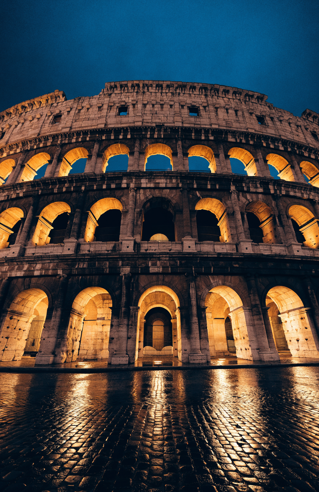 The arches of the Colosseum glow warm gold against a deep Roman night